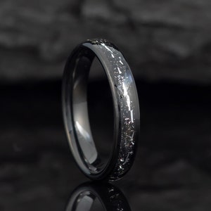 May include: A black tungsten carbide ring with a silver inlay design. The ring has a polished finish and a comfortable fit.