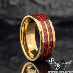 May include: Gold tungsten carbide ring with two red glitter inlay bands. The ring is bevelled and has a brushed finish. "Tungsten Carbide" is engraved on the inside of the band.