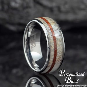 May include: A close-up of a tungsten carbide ring with a polished silver band. The ring features a central inlay of light-colored material with a reddish-brown stripe. The text "Personalized Band" is visible.