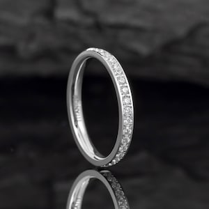 May include: A silver band ring with a row of small, clear cubic zirconia stones set around the entire band.