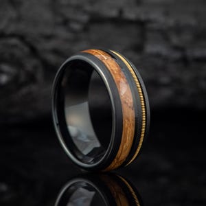 May include: A black tungsten carbide ring with a band of wood and a gold inlay.