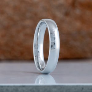 May include: A polished, silver-colored ring with a smooth, rounded surface. The ring is displayed against a neutral background, highlighting its reflective qualities. The ring's design is simple and elegant, suitable for various occasions.