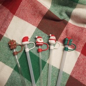 May include: Five clear drinking straws with different Christmas themed toppers. The toppers include a reindeer, Santa Claus, a snowman, Santa Claus, and a gift box.
