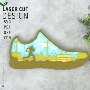 May include: A laser cut design of a running shoe with a cityscape inside. The shoe is yellow and the cityscape is blue and green. The design includes a runner, trees, and a bench. The text "LASER CUT DESIGN" is at the top of the image. The text "SVG, PDF, DXF, CDR" is below the design.