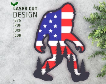 Puede incluir: Un diseño de corte por láser de Bigfoot caminando con el diseño de la bandera estadounidense en su cuerpo. El diseño incluye una silueta de árboles en el fondo.