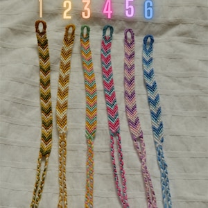 May include: Six colorful friendship bracelets with chevron patterns. The bracelets are made with different colored threads and have tassels at the ends. The bracelets are numbered 1 through 6.