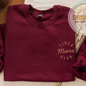 May include: A maroon sweatshirt with the text "Tired Moms Club" embroidered in gold on the front.