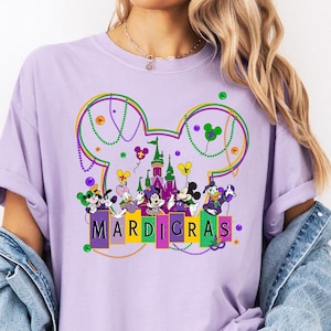 May include: Purple t-shirt with a Mickey Mouse head design featuring Mickey Mouse and friends in Mardi Gras costumes. The design includes the word "Mardi Gras" in colorful blocks.