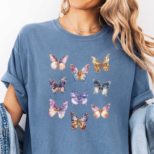May include: A blue t-shirt with a pattern of colorful butterflies. The butterflies are arranged in a grid pattern on the front of the shirt.