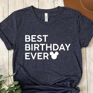 Peut inclure: Un t-shirt gris fonc&eacute; chin&eacute; avec le texte "BEST BIRTHDAY EVER" et une silhouette de Mickey Mouse blanche.