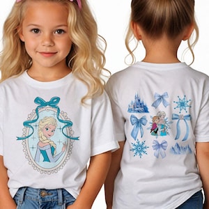 May include: White t-shirts featuring a cartoon image of Elsa from Frozen. The front of the shirt has an oval frame with Elsa, and the back has images of bows, snowflakes, and a castle. The girl is wearing blue jeans and a pink bow.