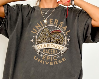 May include: Dark grey t-shirt featuring a graphic of a roller coaster with the text "UNIVERSAL STARDUST RACERS EPIC UNIVERSE" in a vintage style. The shirt has short sleeves and a relaxed fit.