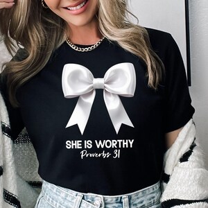 May include: Black t-shirt with a white bow and the text "She is worthy Proverbs 31" printed on the front.