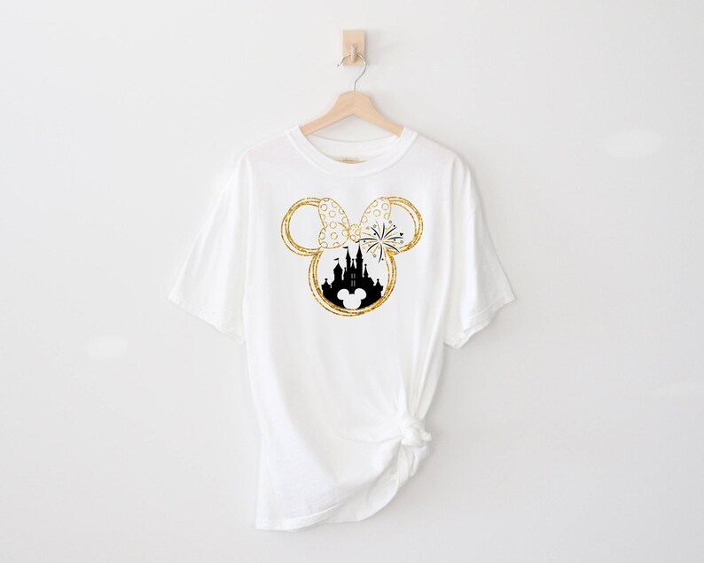 May include: White t-shirt with a gold glitter Mickey Mouse ears design featuring a black silhouette of Cinderella's castle inside the ears.