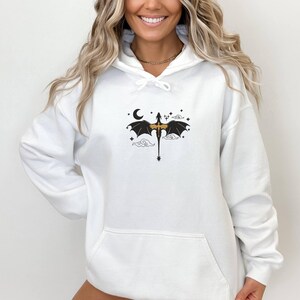 May include: White hoodie featuring a black and gold dragon graphic. The dragon is flying with its wings spread and a crescent moon is in the background.