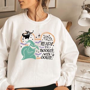Pu&ograve; includere: Felpa bianca con un design di Oogie Boogie color turchese e la scritta "Ready to Boogie with Oogie". Il design include pipistrelli, dadi e Jack Skellington. Una divertente felpa a tema Halloween.
