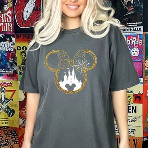 May include: A charcoal grey t-shirt with a gold glitter Mickey Mouse silhouette. The silhouette features a white castle and fireworks inside the ears.
