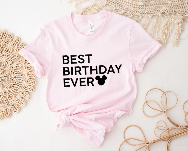 Peut inclure: T-shirt rose avec un texte noir qui dit "Meilleur anniversaire de tous les temps" et une silhouette noire de Mickey Mouse.