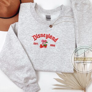 May include: Gray sweatshirt with a red embroidered design that says "Disneyland Est. 1955" with a pair of cherries with pink bows.