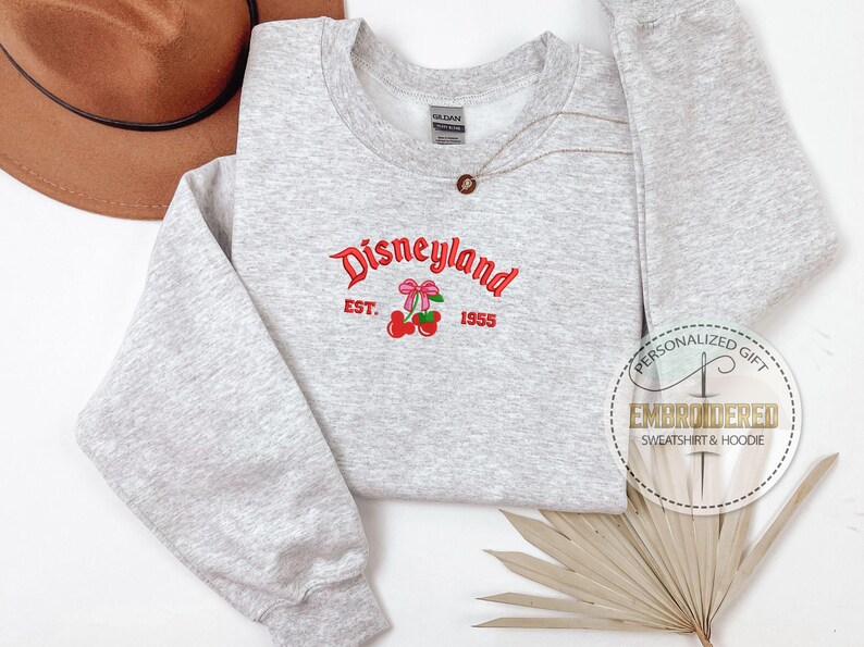 May include: Gray sweatshirt with a red embroidered design that says "Disneyland Est. 1955" with a pair of cherries with pink bows.