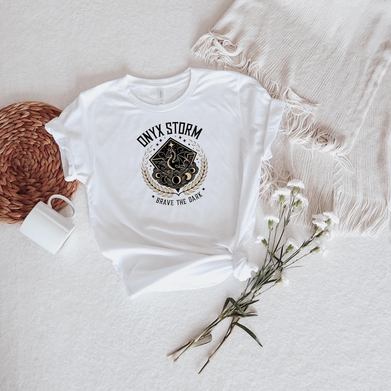 May include: White t-shirt with a black and gold graphic design. The graphic features a stylized dragon with the text "ONYX STORM" and "BRAVE THE DARK".