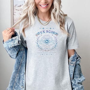 May include: A gray t-shirt with a graphic design of a stylized eye with clouds and leaves. The text "Onyx Storm" is above the eye and the text "I will put out the fire in my soul" is below the eye.
