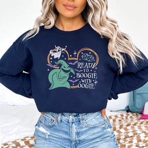 Pu&ograve; includere: Felpa blu navy con una grafica di Oogie Boogie, dadi e pipistrelli, con la scritta "Ready to Boogie with Oogie!". Il disegno &egrave; racchiuso in un contorno di orecchio di Topolino. Un top comodo e casual per Halloween o per i fan Disney.