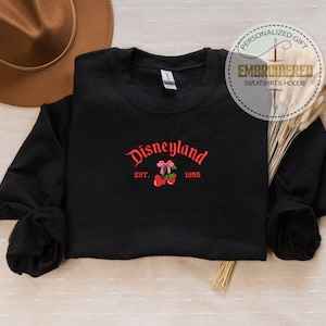 May include: Black sweatshirt with red embroidered text that says "Disneyland Est. 1955" with a red cherry and pink bow.