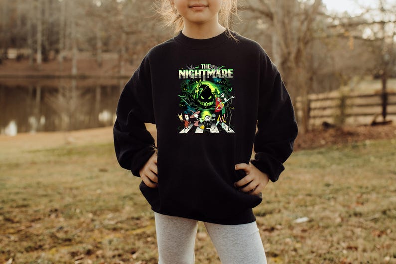 May include: Black sweatshirt featuring a colorful graphic from "The Nightmare Before Christmas." The design includes characters like Jack Skellington and Sally, with the title text "The Nightmare" in green and white.