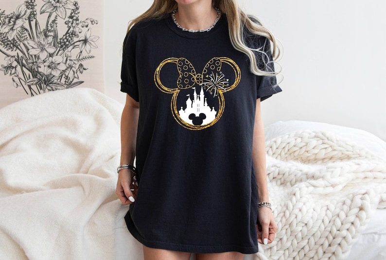 May include: Black t-shirt with a gold glitter Mickey Mouse silhouette featuring a white castle and fireworks inside the ears.