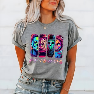 May include: A gray t-shirt featuring a colorful graphic of four horror movie characters. The word "FRIENDS" is printed in a gradient font below the characters. The shirt has short sleeves.