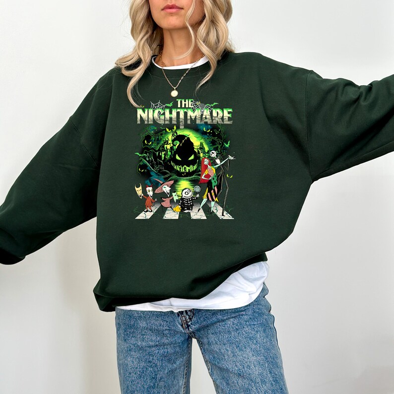 May include: Dark green sweatshirt featuring a graphic from "The Nightmare Before Christmas." The design includes characters crossing a street with the film's title at the top. The sweatshirt is a crew neck style.