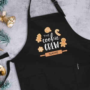 May include: Black Christmas cookie-themed apron with the text "The Cookie Crew" and a rolling pin with the word "NAME" on it.