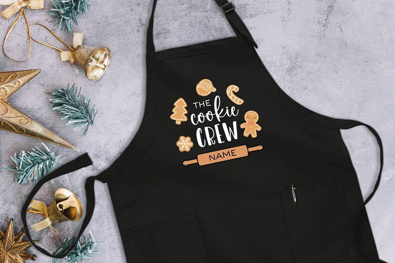 May include: Black Christmas cookie-themed apron with the text "The Cookie Crew" and a rolling pin with the word "NAME" on it.