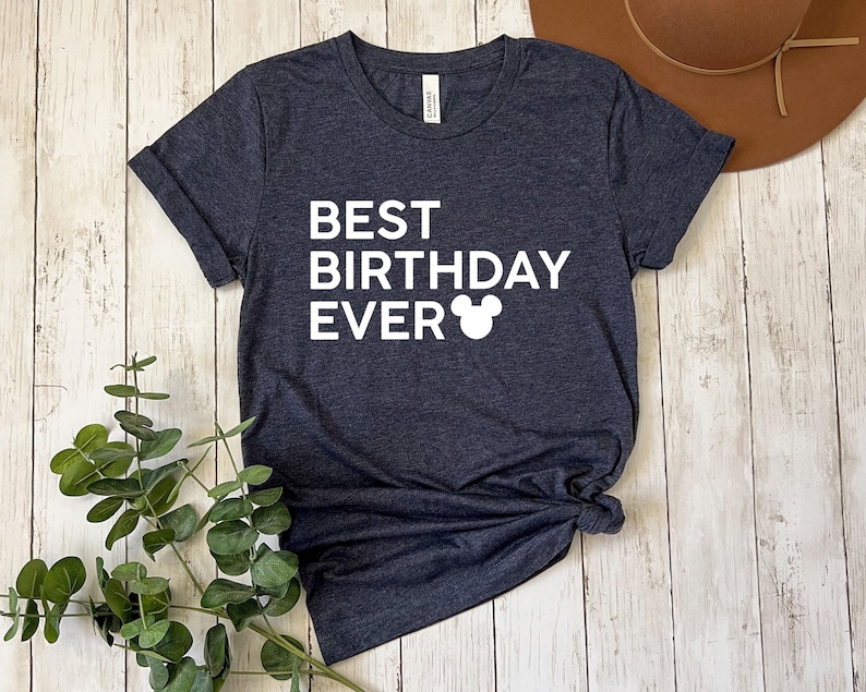Peut inclure: Un t-shirt gris fonc&eacute; chin&eacute; avec le texte "BEST BIRTHDAY EVER" et une silhouette de Mickey Mouse blanche.