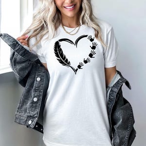 May include: White t-shirt with a black heart design. The heart is formed by a feather and handprints.
