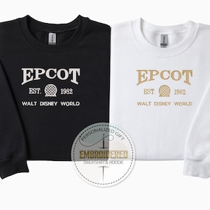 Puede incluir: Sudaderas negras y blancas con el texto "EPCOT EST. 1982 WALT DISNEY WORLD". Las sudaderas tienen mangas largas y cuello redondo. Un logotipo circular dice "PERSONALIZED GIFT EMBROIDERED SWEATSHIRT & HOODIE".