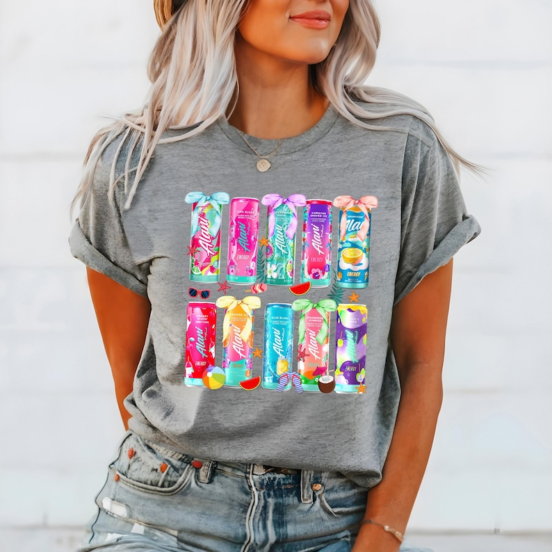 Peut inclure: T-shirt gris avec un motif color&eacute; de douze canettes de boisson &eacute;nergisante. Chaque canette pr&eacute;sente un design diff&eacute;rent avec des fruits tropicaux et des &eacute;l&eacute;ments floraux. Les canettes sont dispos&eacute;es en deux rang&eacute;es, avec des n&oelig;uds et des &eacute;l&eacute;ments d&eacute;coratifs.
