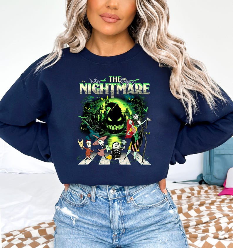 May include: Navy blue sweatshirt featuring a graphic from "The Nightmare Before Christmas." The design includes the text "The Nightmare" above a scene with Jack Skellington, Sally, and other characters crossing a crosswalk in front of a spooky green background.