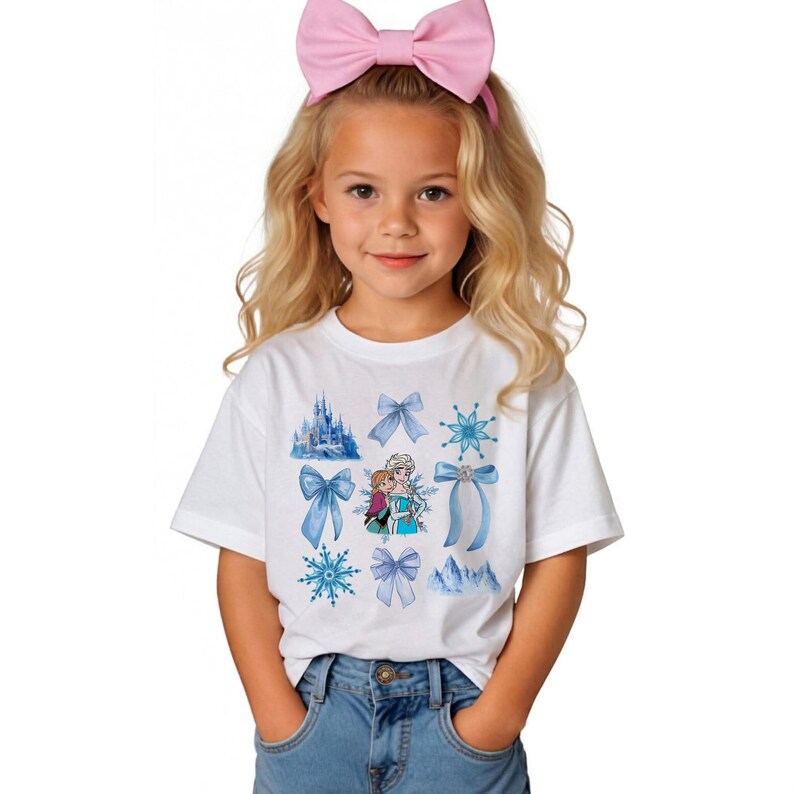 May include: White t-shirt featuring a design with blue bows, snowflakes, and a castle. The shirt also has an image of two characters from the movie Frozen. A pink bow headband is worn by the person in the image.