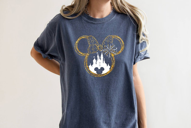 May include: A dark blue t-shirt with a gold glitter Mickey Mouse silhouette design. The silhouette includes a white castle and fireworks.