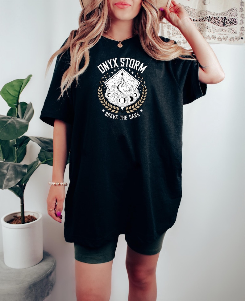 May include: Black oversized t-shirt with a white graphic design featuring a dragon, stars, and the text "ONYX STORM" and "BRAVE THE DARK".