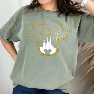 May include: A green t-shirt with a gold glitter Mickey Mouse head design featuring a white silhouette of Cinderella's castle and fireworks.