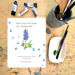 May include: A white instructional sheet titled Paint Your First Texas Bluebonnet! A Beginner Watercolor Tutorial By Cindy Baird, featuring a bluebonnet illustration, surrounded by paint tubes, a gray brush holder, and brushes on a white palette.