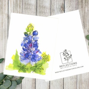 May include: Open greeting card with a watercolour bluebonnet flower illustration. The card shows a detailed image of the flower in shades of purple and blue, with green and yellow accents. The back of the card has a logo and website address.