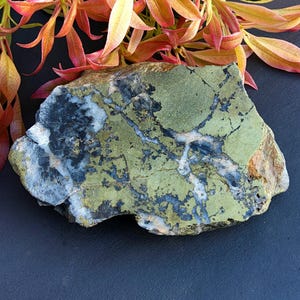 May include: A rough, irregularly shaped piece of green, black, and white stone with a marbled pattern. The stone has a rough, natural texture.