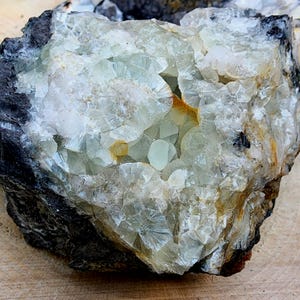 May include: A large, rough, gray rock with a cluster of white and green crystals. The crystals are clustered together in a variety of shapes and sizes.
