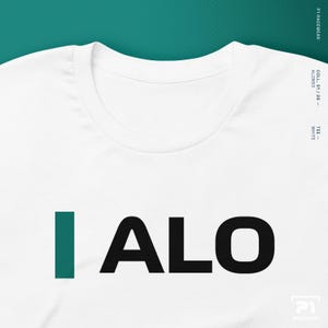 K&ouml;nnte beinhalten: Wei&szlig;es T-Shirt mit dem Text "I ALO" in schwarzen Blockbuchstaben und einem teal "I". Das Shirt hat einen Rundhalsausschnitt und kurze &Auml;rmel. Der Text "COLL S1/26 - ALONSO" ist vertikal auf der rechten Seite aufgedruckt.