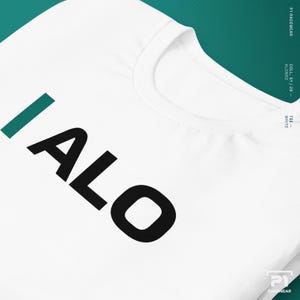 K&ouml;nnte beinhalten: Wei&szlig;es T-Shirt mit dem Wort "ALO" in gro&szlig;en schwarzen Buchstaben und einem gr&uuml;nen vertikalen Strich. Das Shirt hat einen Rundhalsausschnitt und ist aus einem weichen Material. Der Text "TEE - WHITE" ist seitlich aufgedruckt.