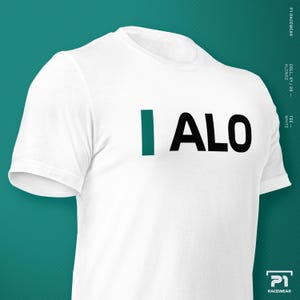 K&ouml;nnte beinhalten: Wei&szlig;es T-Shirt mit dem Text "I ALO" in Schwarz und Teal. Das Shirt hat kurze &Auml;rmel und einen Rundhalsausschnitt. Der Text ist mittig auf der Brust platziert. Der Hintergrund ist teal.